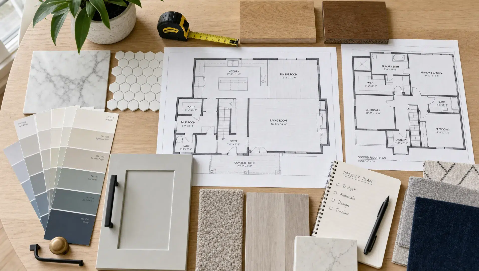 A renovation planning table with floor plans, wood samples, tile pieces, paint swatches, measuring tools, and labeled material samples arranged neatly for a home remodeling project, viewed from above in a bright room.